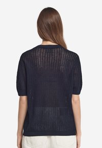 Marinblå stickad tröja med korta ärmar, med en lös väv och ribbad halsringning och nederkant. Baksidan är halvgenomskinlig.