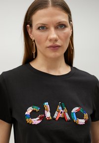 Svart bomullströja med ordet "CIAO" i färgglada, texturerade detaljer. Korta ärmar och design med rund hals.