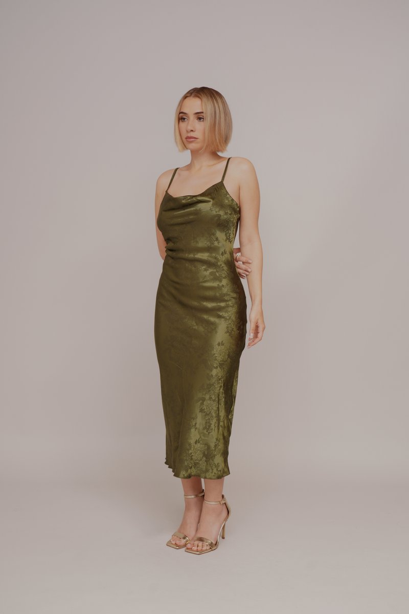 Satin midi-kjole i olivengrønn med tynne stropper, drapering i halsen og blomstermønster. Kombinert med gullfargede sandaletter med stropper.