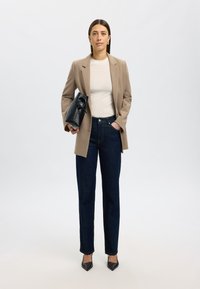 Beige kavaj, vit t-shirt och mörkblå jeans. Håller en svart handväska. Spetsiga svarta klackar. Enkel, skräddarsydd design och texturer.