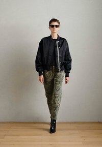 Crna bomber jakna s srebrnim detaljima, u paru s maslinasto-zelenim hlačama sa zebraste uzorke i crnim uštipom čizmama.
