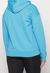 Ljusblå hoodie i mjukt tyg, med huva, ribbade ärmslut och nederkant, samt en avslappnad passform. Bärs med svarta leggings.