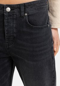 Vaqueros de mezclilla negros con un diseño ajustado, estilo clásico de cinco bolsillos y herrajes metálicos plateados en la cintura.