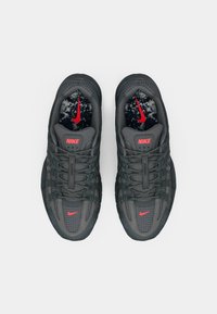 Nike sneakers with a dark gray mesh upper, featuring red accents and logo, textured rubber sole, and checkered pattern elements.