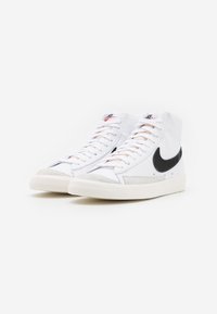 Höga sneakers i vitt läder med en svart swoosh, ljusgrå accenter och platta snören. Har en texturerad gummisula.