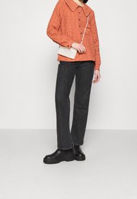 Orange tekstureret bluse med en stor krave, parret med sorte lige ben jeans og kraftige sorte støvler. Hvid crossover taske er inkluderet.