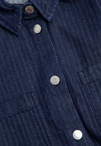 Donkerblauwe denim shirt met visgraatpatroon, voorzien van zilveren drukknoopsluiting en twee borstzakken. Gestructureerde stof, gestructureerde kraag.