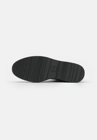Suela de zapato de goma negra con ranuras horizontales y un logo circular. Presenta un diseño plano y bordes ligeramente elevados para un mejor agarre.
