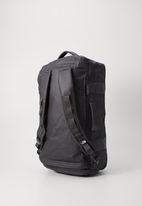 Black backpack with a rectangular shape, synthetic material, padded shoulder straps, and a side zipper pocket. Features a logo on the strap.