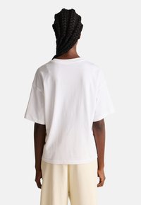 Camiseta de algodón blanca con un ajuste holgado, mangas cortas y escote redondo. Textura suave, con un diseño liso y sin logotipos visibles.