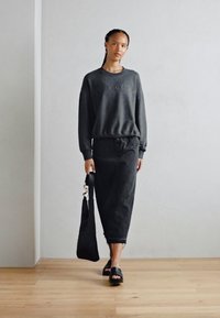 Felpa nera con testo in rilievo, gonna nera coordinata e sandali aperti. La modella porta una borsa a spalla nera dalla texture particolare.