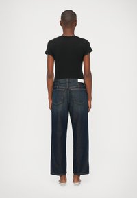 Camisa negra de manga corta combinada con pantalones vaqueros de pierna ancha en azul oscuro. Los vaqueros tienen bolsillos traseros y una etiqueta blanca en la cinturilla.