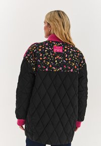 Prešívaná čierna bunda s kvetinovým vzorom na ramennom diele, ružovým rebrovaným golierom a manžetami a štítkom na chrbte.