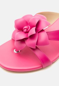 Φωτεινό ροζ σανδάλι με φαρδιά λουρί και μεγάλη στρωματοποιημένη διακόσμηση λουλουδιού στην περιοχή των δαχτύλων, λεία σόλα και μπεζ εσωτερική επένδυση.
