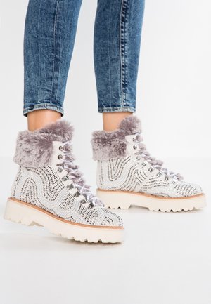 Bottes d'hiver blanches avec des clous argentés, une bordure en fourrure grise et des semelles épaisses portées avec un jean bleu retroussé.