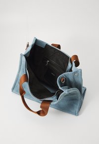 Denim tote taske med brune læderhåndtag. Indersiden har en sort foring, en lynlåslomme og rigeligt plads til genstande. Lynlåslukning på toppen.