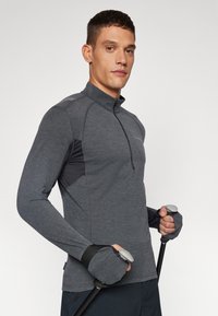 Gray long-sleeve athletic top with a high collar and half zip. Features contrasting dark mesh panels and thumbholes. Model holds poles.