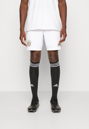 Shorts da calcio bianchi con logo dorato del Bayern Monaco, calze nere fino al ginocchio con strisce bianche e scarpini neri con dettagli blu.