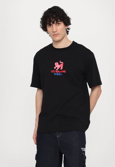 T-shirt en coton noir avec un graphisme rouge et bleu, portant le texte "LES BENJAMINS" et une illustration stylisée d'un lion sur la poitrine.