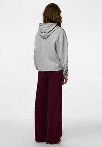 Szara bluza z kapturem o luźnym kroju, zestawiona z szerokimi bordowymi spodniami z miękkiego materiału. Prosty, casualowy design.