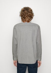 Chemise à manches longues gris clair en tissu doux, avec un ourlet en courbe, des poignets fixés par des boutons et un design de col simple.
