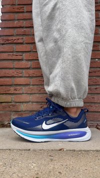 Pantof de alergare cu partea superioară bleumarin, logo Nike alb și accente gri vizibile. Dispune de o talpă groasă mov și albă cu branding „ZOOMX”.