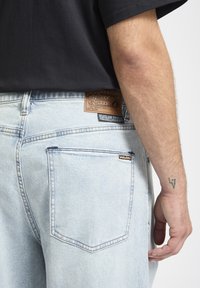 Lyseblå denimjeans med rett passform, med en brun lærpatch, to baklommer og en vevd logomerke nær midjen.