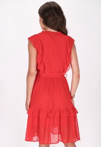 Rotes gepunktetes Kleid mit Rüscheärmeln, elastischem Taillenbund und mehrstufigem Rüschensaum. Durchscheinende Textur mit einem leichten, fließenden Design.