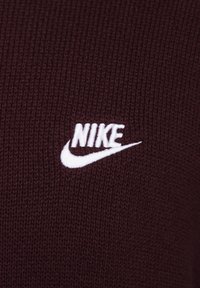 Burgundské pletené látky s bílým vyšitým logem Nike. Textura je žebrovaná, což zvyšuje vizuální přitažlivost látky.