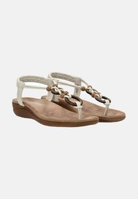 Sandalias de color beige claro con plantilla acolchada, que presentan una suave correa elástica en la parte posterior y nudos decorativos en tonos marrón y tostado.