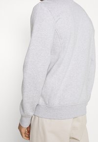 Grå sweatshirt med ribbad krage och muddar, med en enkel design och mjuk textur, visad bakifrån.