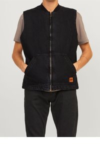Czarna dżinsowa kamizelka z zamkiem z przodu, dwoma przednimi kieszeniami i małym pomarańczowym logo po lewej stronie. Nosi się ją na szarej koszulce z krótkim rękawem.