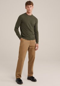 Olívazöld pulóver kerek nyakkal és szűkített mandzsettával, világosbarna chinos nadrággal és fránkos fekete loafer cipővel párosítva.