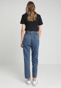 Jeans de mezclilla azul de cintura alta con pierna ajustada, bolsillos traseros y un ligero desgaste. Combinados con una camiseta negra de manga corta y zapatillas blancas.