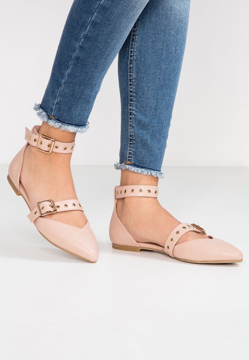 Bailarinas de punta afilada en rosa claro, con tiras alrededor del tobillo, que presentan un hebilla y acentos de tachuelas circulares. Material de cuero suave, con tacón bajo.