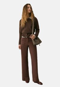 Maglione marrone a maglia con collo rotondo e bordo con bottoni, abbinato a pantaloni marroni a gamba larga. Borsa e scarpe marroni coordinate.