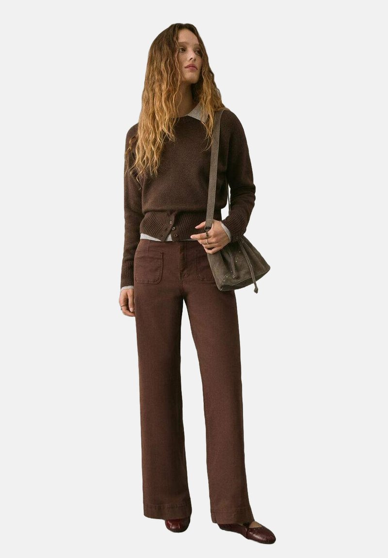 Maglione marrone a maglia con collo rotondo e bordo con bottoni, abbinato a pantaloni marroni a gamba larga. Borsa e scarpe marroni coordinate.