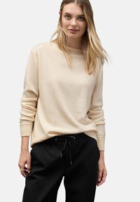 Cremefarbener, langärmeliger Strickpullover mit gerippten Bündchen und lockerer Passform, kombiniert mit schwarzen Jogginghosen mit Kordelzug. Einfaches und minimalistisches Design.