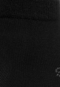 Schwarze Socke mit geripptem Muster und elastischem Bündchen. Verfügt über ein rundes Logo in einer helleren Farbtone. Das Material scheint weich und flexibel zu sein.