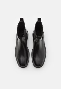 Černé kožené kotníkové boty s hladkým povrchem, elastickými bočními panely a prošíváním podél podešve. Pohled zvrchu ukazuje minimalistický design.