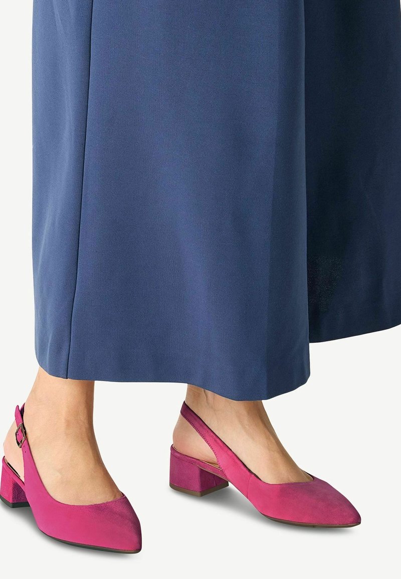 Pieds portant des talons blocs à bride arrière en daim rose, associés à un pantalon large bleu.