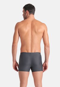 Costume da bagno da uomo grigio scuro, realizzato in materiale liscio, con una vestibilità a vita media, una semplice vita elastica e senza motivi visibili.