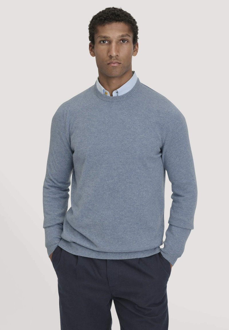 Lichtblauwe trui van zachte gebreide stof, met een ronde hals en geribde manchetten. Gedragen over een overhemd met kraag, met een relaxte pasvorm.