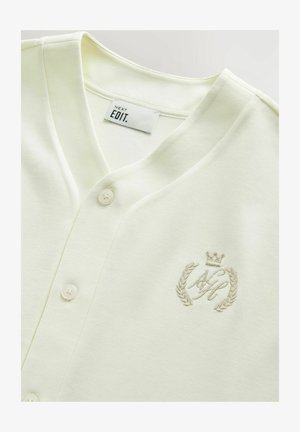 Šviesiai geltonas medvilninis kardiganas su V formos iškirpte, turintis mygtukus ir siuvinėtą logotipą su karūna ir laurų vainiku.