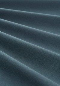 Teksturowana ciemnozielona tkanina z diagonalnymi fałdami, charakteryzująca się gładką powierzchnią i subtelnym wzorem splotu, idealna do tapicerki lub zasłon.