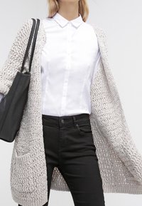 Ljusgrå stickad cardigan med öppen front, texturerat tyg, två fickor; bärs över en vit skjorta med knappar och svarta byxor. Svart väska ingår.