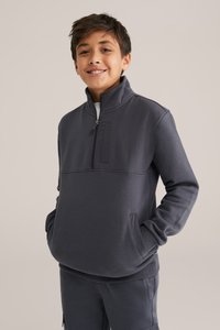 Pulover gri închis cu fermoar, fabricat dintr-un material moale, cu un guler înalt, buzunar frontal și manșete cu model în relief. Asortat cu pantaloni corespunzători.