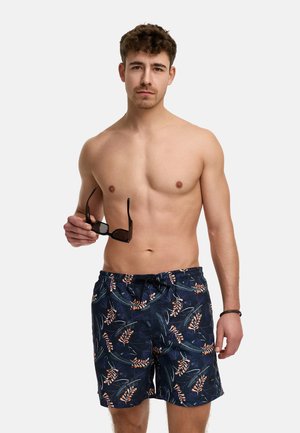 Simshorts med en mörk marinblå bakgrund och ett tropiskt blommönster i orange och grönt. Tillverkade av lätt, snabbtorkande material.