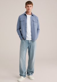 Světle modrá košile s knoflíky a dvěma kapsami na prsou přes bílé tričko, doplněná volnými světle modrými džíny a bílými teniskami.