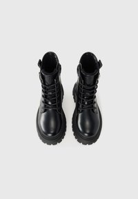 Botas de tobillo negras con cordones y suela gruesa, parte superior de piel suave, acentos texturizados y cremallera lateral para facilitar el uso.